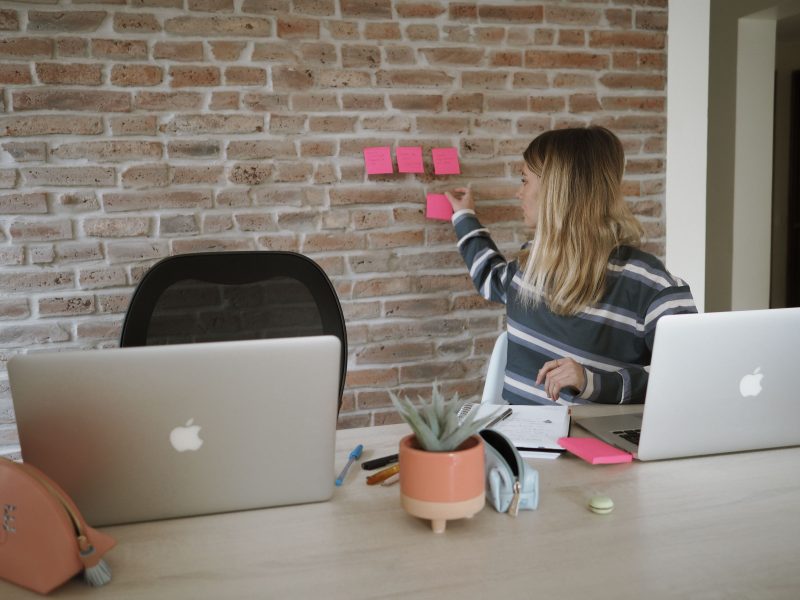 mujer trabajando en un notebook y colocando post it en una pared